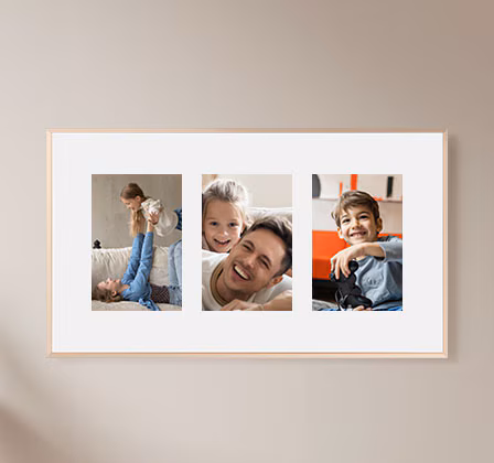 The Frame TV hangs on a wall, displaying three different family pictures on a white matte background.